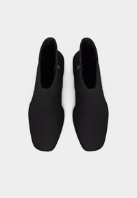 Ζευγάρι μαύρων μποτών αστραγάλου με πλαϊνά φερμουάρ, τετράγωνες μύτες και ομαλή υφή, σε άποψη από πάνω σε ανοιχτό φόντο.