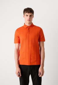 Polo de manga curta em laranja brilhante, feito de um tecido texturizado com um padrão de diamante, apresentando um colarinho e uma ''placket'' com três botões.