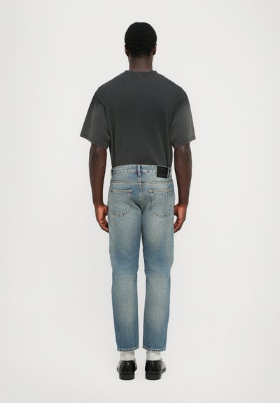 Gray short-sleeve t-shirt paired with light blue jeans featuring a straight fit and back pockets. Black label at the waistband. Black shoes.