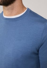 Pull bleu en tricot avec un col rond et des manches longues, présentant une texture lisse et un design près du corps.