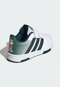 Biele tenisky s zelenými akcentmi, tromi čiernymi pruhmi a rozprávkovou postavičkou na päte. Obsahuje pásik na suchý zips na zapínanie.