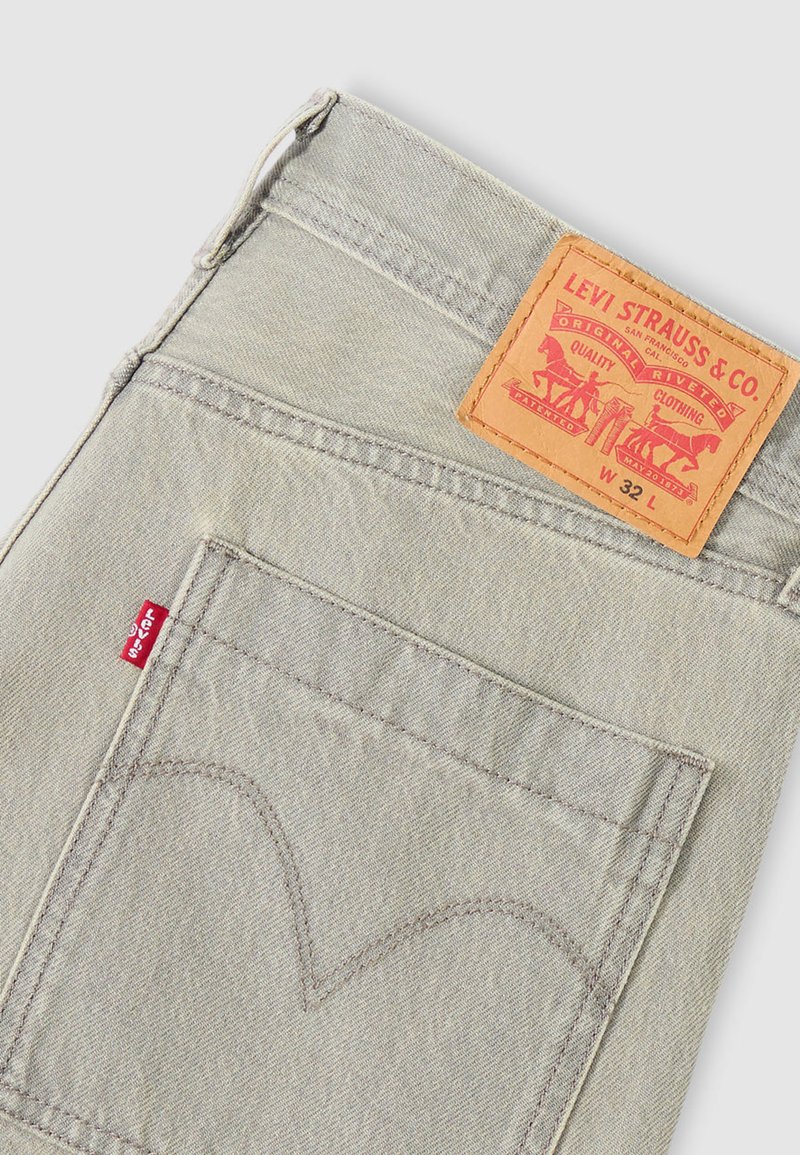 Hellgraue Denim-Jeans mit einer markanten Lederapplikation und rotem Markenlogo. Auffällige Rückensteppung in geschwungenem Design.