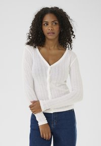 Vit stickad cardigan med V-hals, långa ärmar och knappstängning, med ribbad textur och subtila mönsterdetaljer.