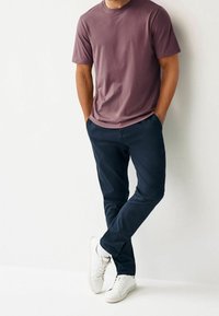 Tílko s krátkým rukávem a kulatým výstřihem v barvě mauve, kombinované s námořnickými kalhotami a bílými teniskami. Oblečení má volný střih a jednoduchý design.