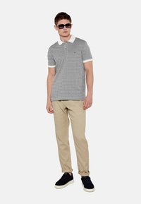 Polo de rayas en blanco y negro con un collar blanco, combinado con pantalones beiges y zapatillas negras. El modelo lleva gafas de sol oscuras.