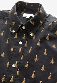 Chemise noire à boutons avec un motif d'arbre de Noël doré métallique. Elle présente des boutons blancs et un col classique.