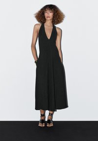 Black halter neck dress with a deep V-neckline, wide legs, and pockets. The fabric appears textured, enhancing its overall design.