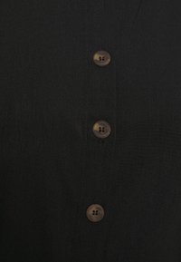 Svart skjorta med en slät textur, knapplist, fyra bruna knappar och subtila stygn över tyget.