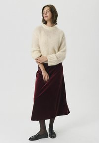 Suéter crema con una textura suave y peluda, combinado con una falda de terciopelo burdeos oscuro. El modelo lleva zapatos tipo mocasín negros y medias negras.