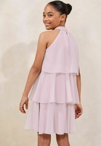Rochie roz deschis, cu straturi, realizată dintr-un material fluid. Are un guler halter și straturile creează un efect moale de plisare.