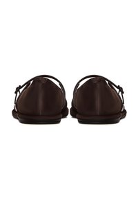 Pantofole marroni, in morbido camoscio, con punta arrotondata, dettaglio posteriore con cinture sottili e fiocchi, suola piatta, design minimale.