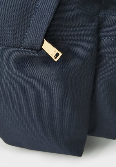 Sac en tissu navy avec une finition texturée, doté d'un tirette dorée. Le design est rectangulaire avec des coutures visibles et des détails.
