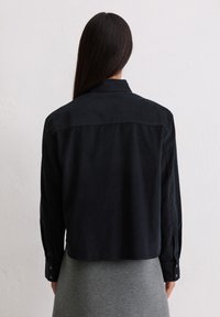 Chemise noire à manches longues avec col chemise et poignets à boutons, en tissu lisse, avec une coupe droite à l'ourlet.