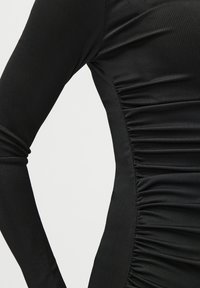 Μαύρη ριγωτή μπλούζα με μακριά μανίκια και λεπτομέρεια τσαλακωμένη στο πλάι. Η λεία υφή και η εφαρμοστή γραμμή ανα�δεικνύουν τη γραμμή του ρούχου.