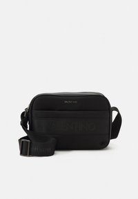 Μαύρη τσάντα χιαστί με υφασμάτινη υφή, κλείνει με φερμουάρ, ορθογώνιο σχήμα, ιμάντας με υφή που φέρει ανάγλυφο λογότυπο, μινιμαλιστικός σχεδιασμός, χωρίς ορατές διακοσμήσεις.