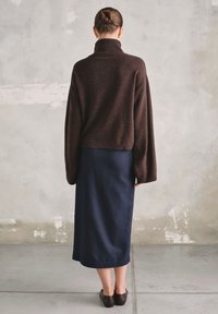 Brązowy sweter z golfem z wełny, zestawiony z granatową spódnicą do kostek. Materiał wydaje się miękki, a design zawiera szerokie rękawy i prążkowane wykończenia.
