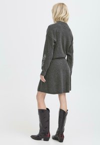 Abito grigio lavorato a maglia con maniche lunghe, caratterizzato da ricami floreali sulle maniche. Abbinato a stivali da cowboy neri in pelle al ginocchio.