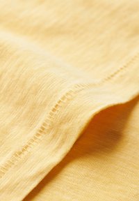 Geel katoen stof met een gladde textuur, voorzien van subtiele kleurvariaties en een keurig gestikte rand.