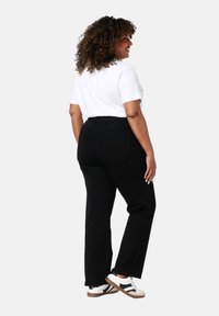 Pantalons en denim noir avec une coupe droite, dotés de poches arrière et d'une taille haute, associés à un t-shirt blanc et des baskets décontractées.