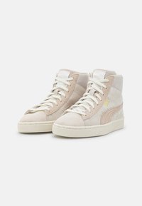 Wysokie sneakersy z beżowego zamszu, z białymi sznurowadłami, teksturowaną gumową podeszwą oraz złotymi detalami z logo po boku.