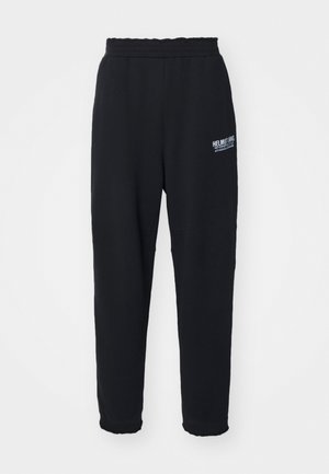 Svarte joggebukser laget av myk stoff, med stretch midjebånd, smale ben, og en liten hvit logo på venstre side.