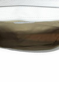 Wnętrze białej skórzanej torebki z gładką beżową podszewką. Posiada zamek błyskawiczny i minimalne detale. Prosty design i przestronność.