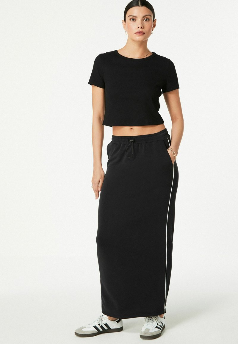 Sort cropped t-shirt og lang sort nederdel med snøre. Nederdelen har hvide sidelister. Modellen bærer hvide sneakers.