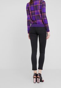 Suéter de cuadros morados con pantalones negros ajustados. Los pantalones tienen un corte slim, y la modelo lleva unos tacones negros con acentos rosas.