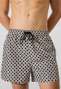 Mustvalged ujumispüksid, millel on ruudustiku muster tähtedega, elastne vöökoht ja nööriga tõmblukk. Valmistatud kergest materjalist.