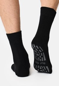 Sorte ankelsokker med ribbede manchetter, der har et tekstureret gråt grebsmønster under foden for forbedret trækkraft.