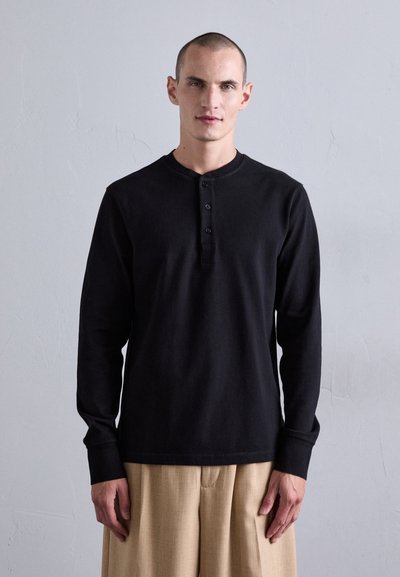 Sort langærmet henley skjorte med runde halsudskæring og placket med tre knapper. Stoffet virker blødt med en glat tekstur.