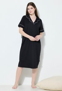 Vestito da notte nero in tessuto morbido, con collo a camicia, maniche corte, dettagli in piping bianco e design fino al ginocchio, esposto su uno sfondo semplice.