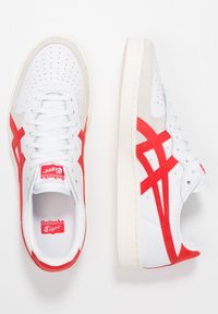 Vita sneakers med grå mockadetaljer och röda överlägg. Har perforerat tå, vita snören och 'Onitsuka Tiger'-logotyp på tungan.