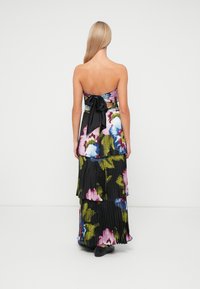 Robe maxi sans bretelles avec un motif floral coloré sur fond noir, présentant un design plissé et un nœud noir à l'arrière.