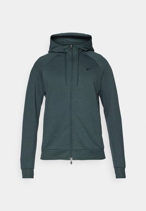 Hættejakke med lynlås i mørk teal, lavet af blødt materiale med raglanærmer, en frontlynlås, justerbare snore og et sort logo.