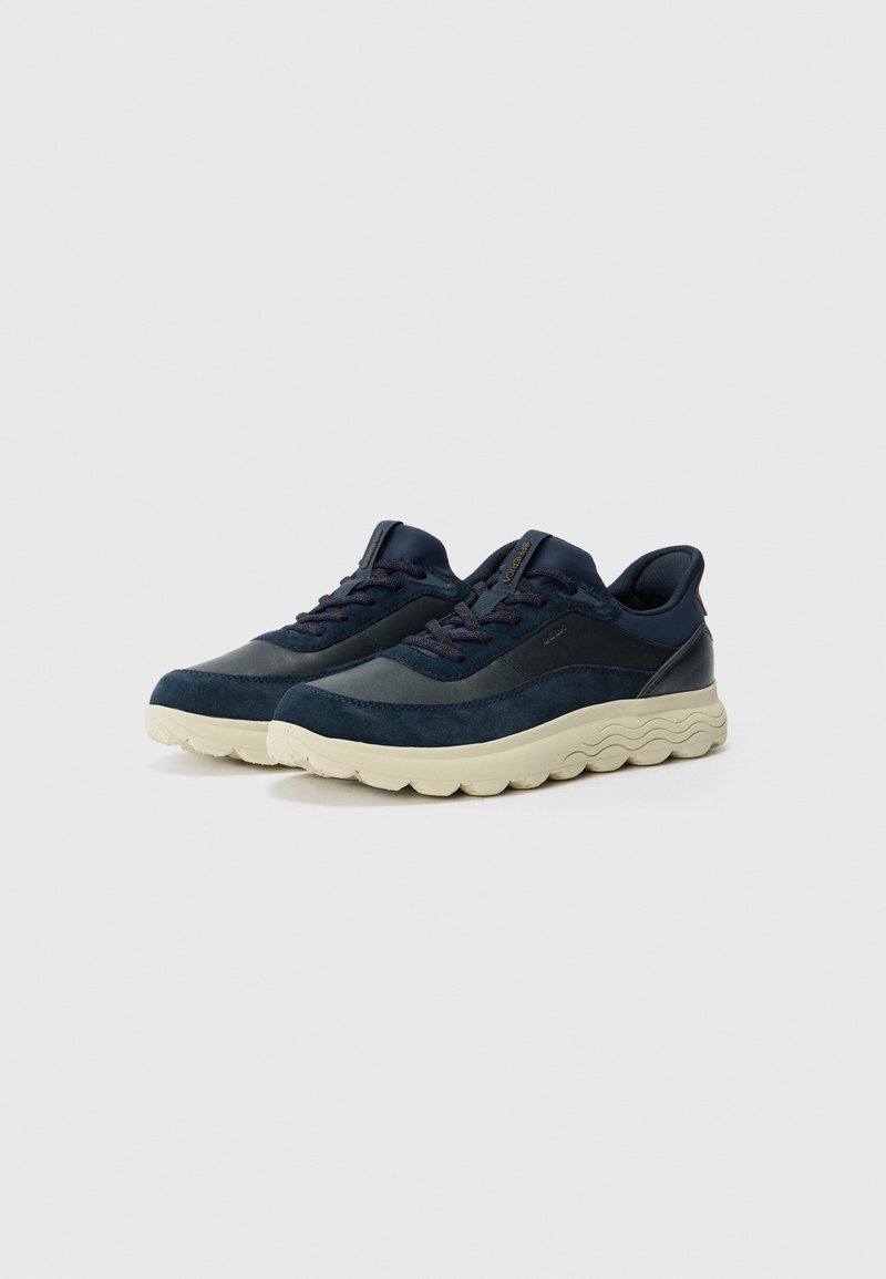 Zapatillas azul marino con parte superior de ante y cuero, suela de goma crema, cierre de cordones, cuello acolchado y diseño texturizado en la suela.