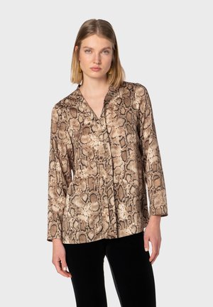 Snake print long-sleeve blouse in beige and brown tones. Features a V-neck, smooth fabric, and a loose fit, paired with black trousers.