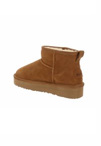 Stivale alla caviglia in suede marrone con fodera in shearling, punta rotonda e suola in gomma resistente. Presenta un linguetta posteriore e dettagli cuciti.