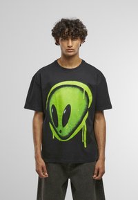 Sort bomulds T-shirt med et stort grønt aliengrafik på fronten. Designet inkluderer sorte accenter og en afslappet pasform.