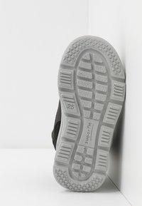 Calzature nere con suola in gomma testurizzata, caratterizzate da profondi pattern di battistrada e un'etichetta del marchio "superfit" vicino al tallone, angolate su uno sfondo bianco.