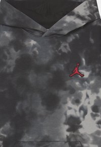 Sweatshirt à capuche en gris et noir avec un motif tie-dye, comportant un logo Jumpman rouge brodé sur la poitrine. Tissu doux avec une coupe décontractée.