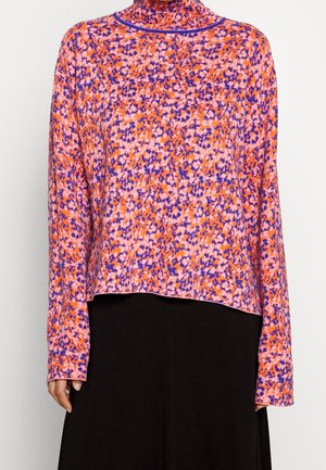 Blouse met lange mouwen en col met abstract bloemmotief in oranje, roze en paars, gedragen met een zwarte rok.