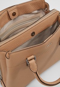 Läderhandväska i tan med en texturerad yta, som har en magnetisk knappstängning och flera innerfack, inklusive fickor med dragkedja.