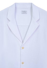 Chemise en lin blanche avec un col cranté, deux boutons jaunes et une étiquette portant la mention "CALLIOPE" ainsi que "COMFORT FIT". Texture lisse.
