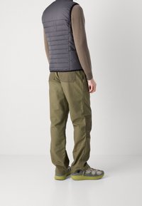 Vad som ser ut som en grå vadderad väst över en brun tröja, kombinerad med olivgröna cargobyxor och grå sneakers med gröna sulor, vilket visar en avslappnad utomhusstil.