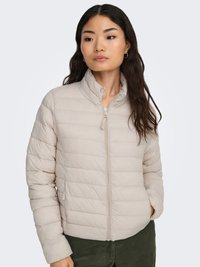 Beige, gesteppte, leichte Jacke mit hohem Kragen, durchgehendem Reißverschluss und gerippten Bündchen, kombiniert mit strukturierten, grünen Cordhosen.