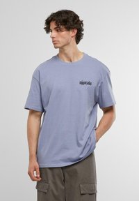 Tricou din bumbac de culoare lila deschis, cu guler rotund și mâneci scurte, având un text negru în zona din stânga a pieptului. Croi lejer.