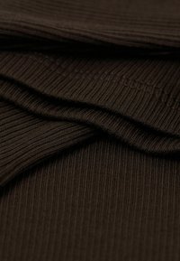 Hnědá žebrovaná tkanina, která ukazuje texturu a hloubku, s vrstvenými záhyby zdůrazňujícími pružnost a tloušťku materiálu.