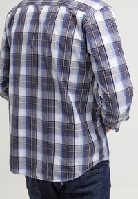 Ruudullinen paita, jossa on sekoitus laivastonsinistä, valkoista ja vaaleansinistä väriä. Valmistettu kevyestä kankaasta, jossa on nappikaulus ja kaareva helma.