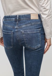 Granatowe dżinsy o slim fit, z dwoma tylnymi kieszeniami i brązową skórzaną metką na pasku. Gładka tekstura i klasyczny design.